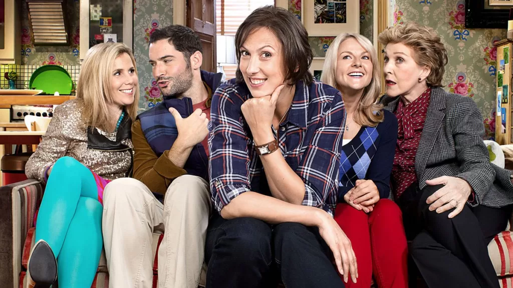 Five actors from the British show MIRANDA. A woman is sitting forward on a couch giving a vexing smile.